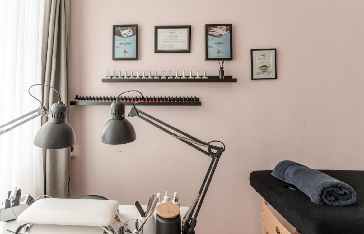De behandelruimte van KiSO beauty: roze muur met certificaten, planken vol nagellak en een behandelbank