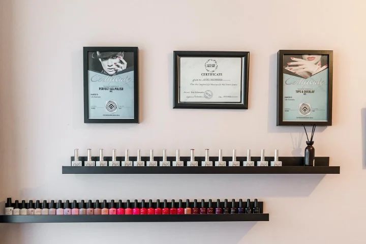 Certificaten aan de roze muur boven twee planken nagellak